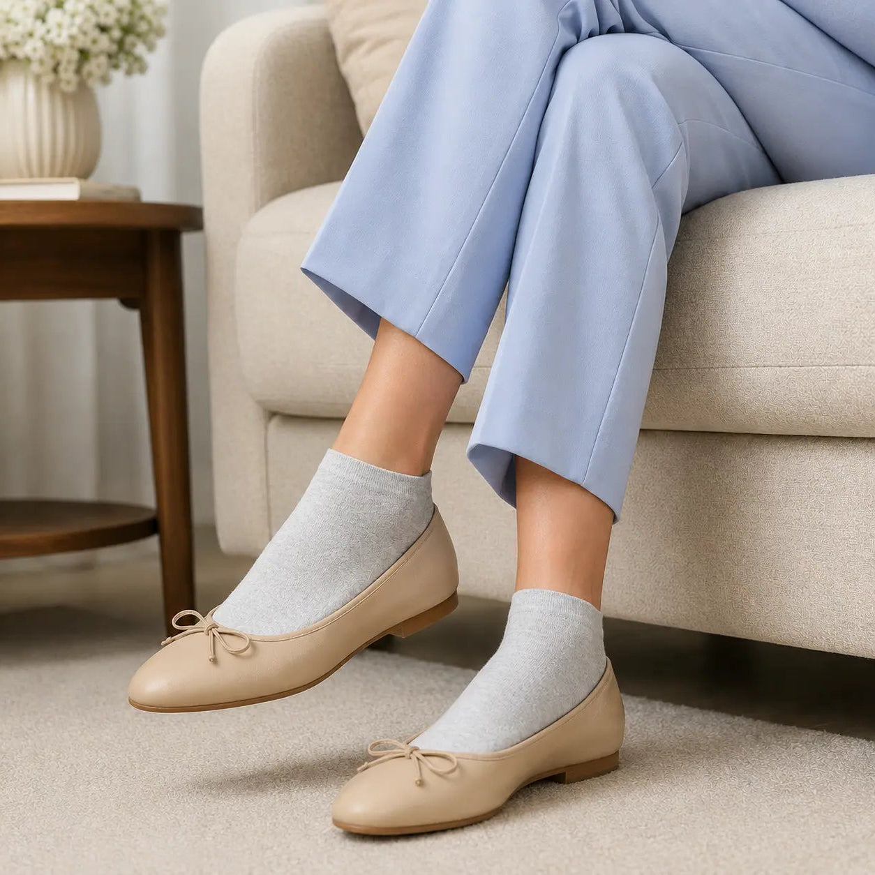 Person wearing beige flats and light gray socks sitting on a beige couch.