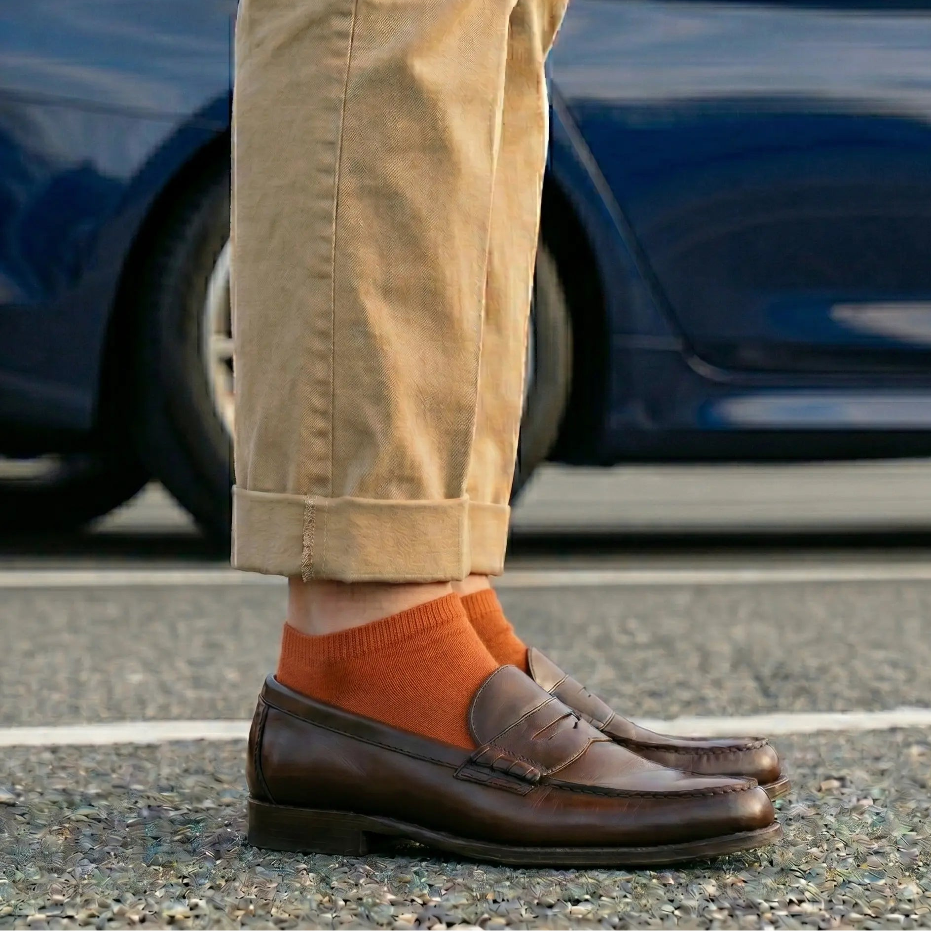 Person wearing brown shoes and orange socks standing on a road with a blurred car in the background.