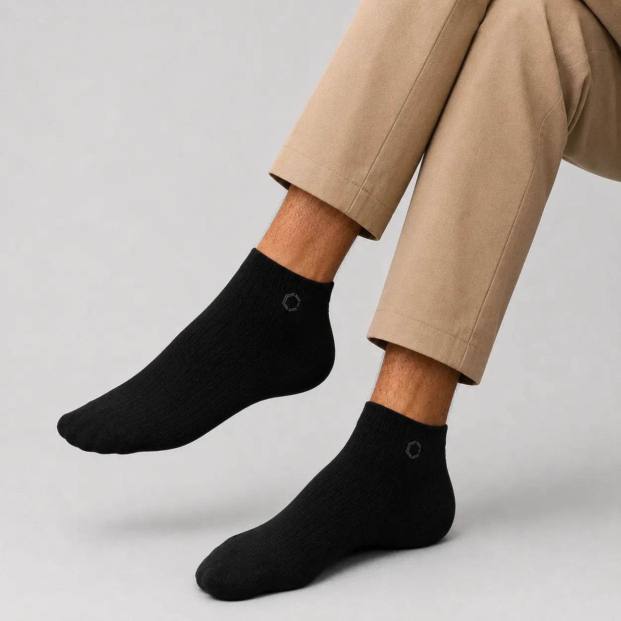 Black ankle socks worn with beige pants on a light gray background