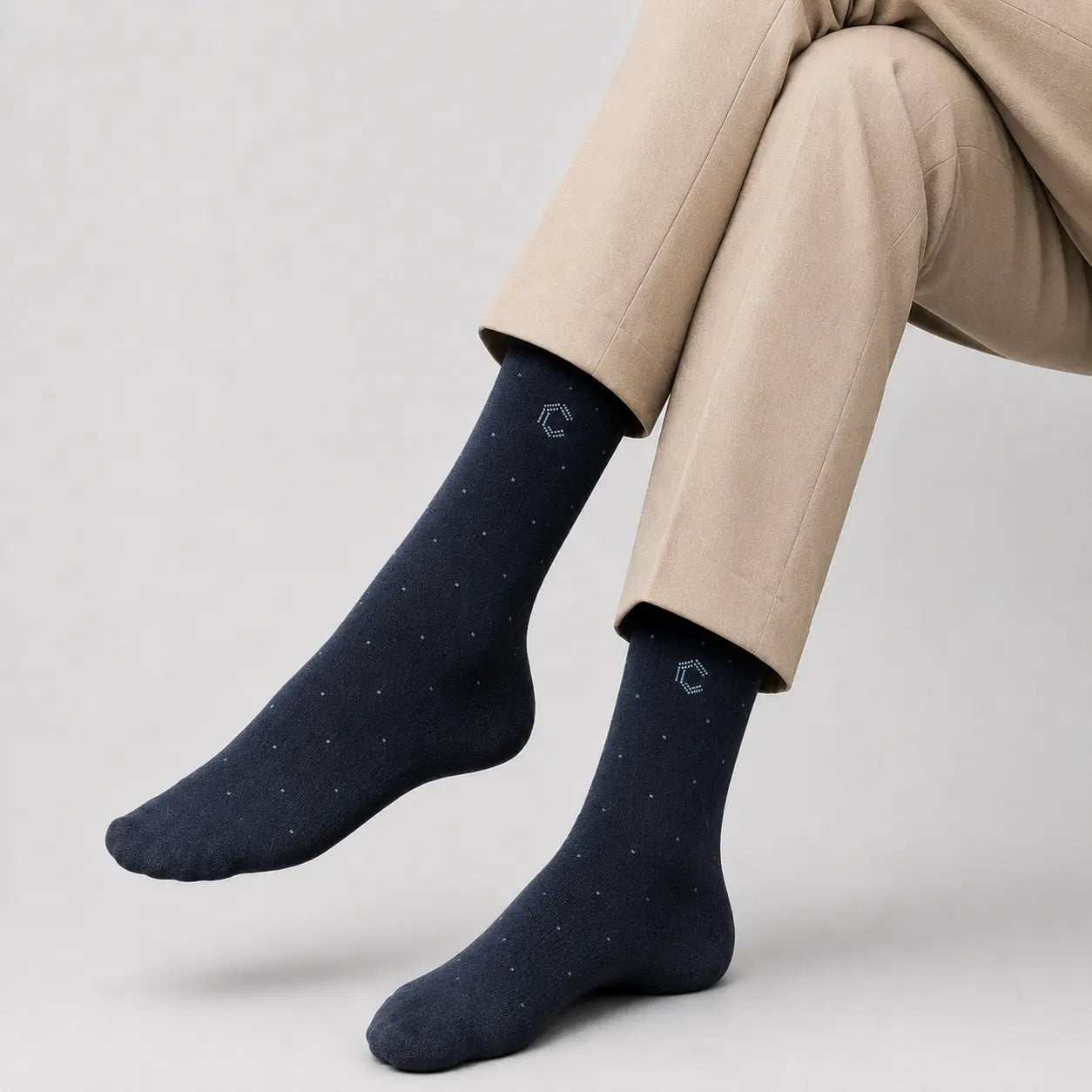 Navy blue socks with a subtle pattern worn with beige pants on a light gray background