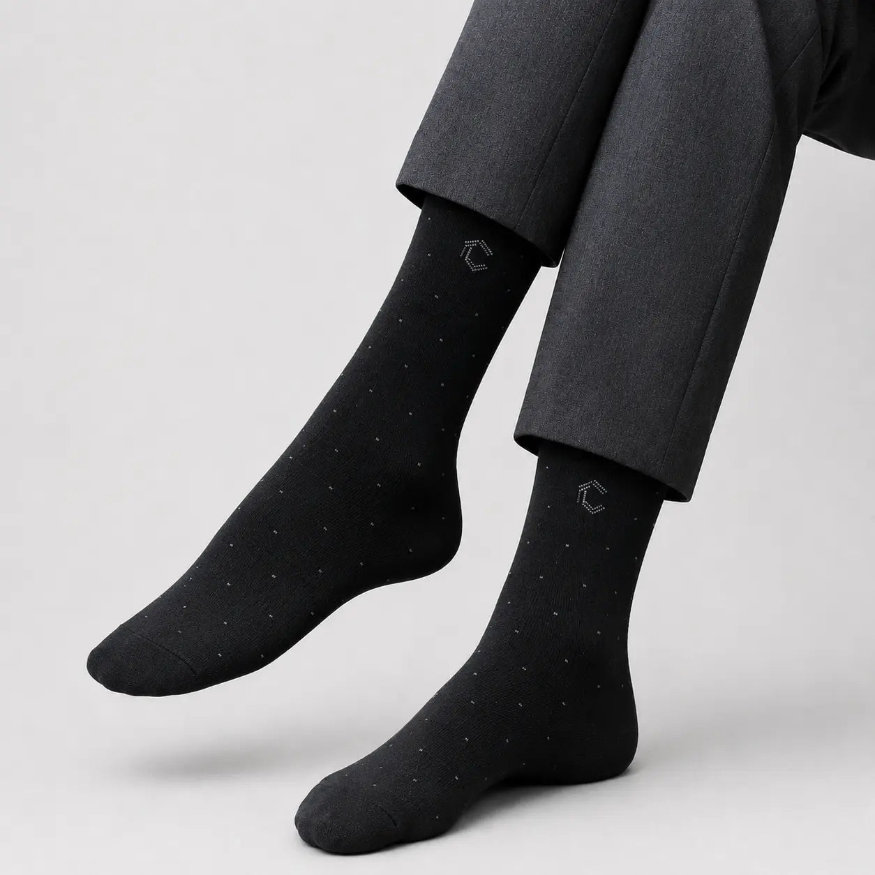 Black socks with subtle pattern worn with gray pants on a light gray background
