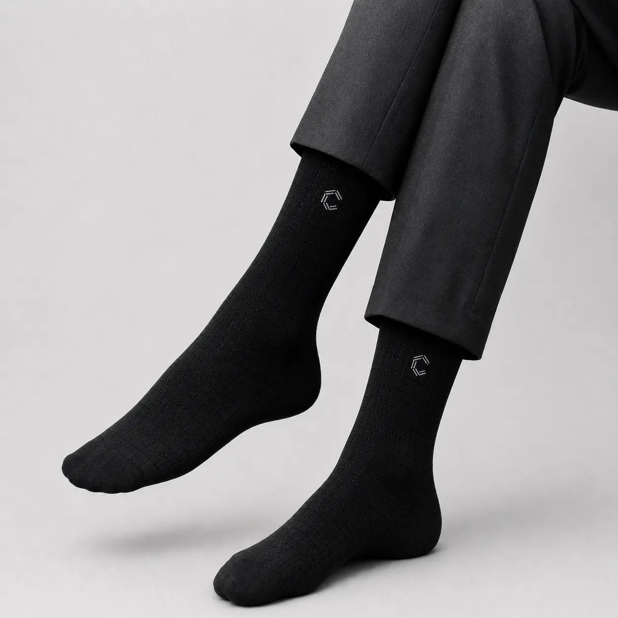 Black socks with a logo worn by a person in a suit on a light gray background